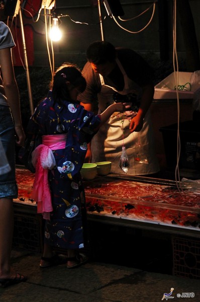A child dressed in traditional yukata plays kingyo sukai the goldfish scooping game at a summer matsuri festival in Japan